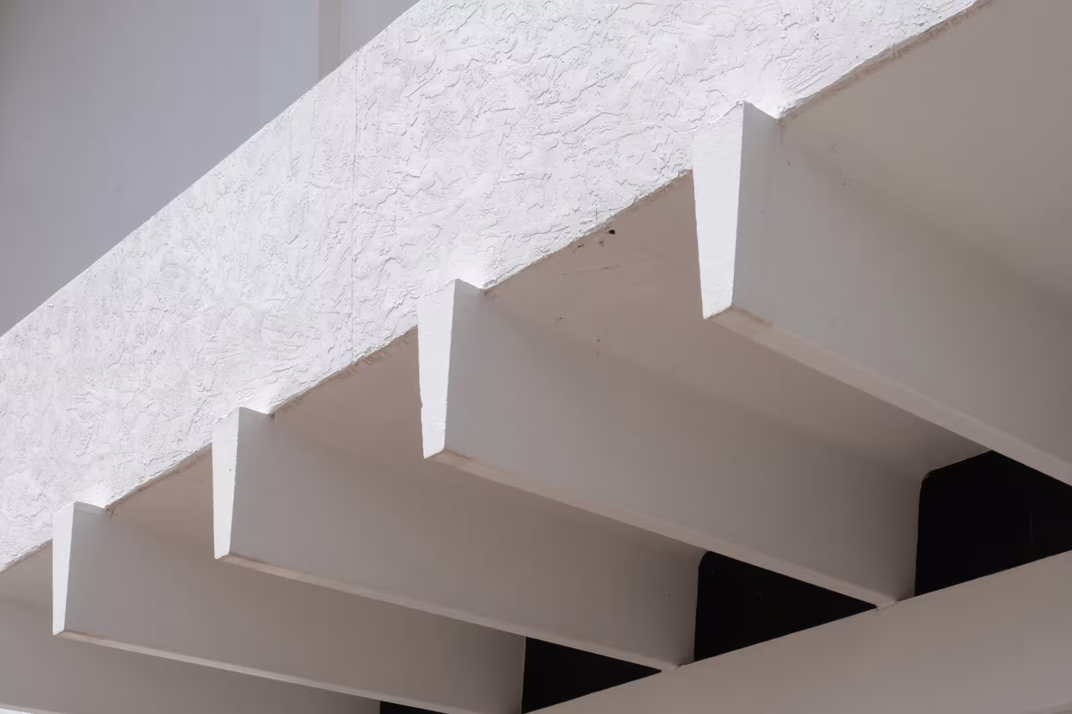 Close-up of white concrete overhang with exposed beams and textured stucco surface, showing bold geometric lines in modernist architectural style.