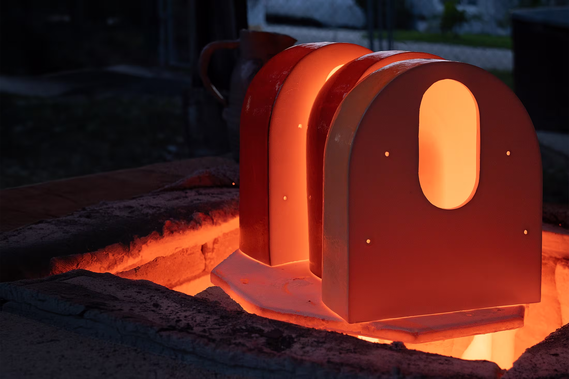 Glowing ceramic sculptures with arch shapes in an outdoor kiln during the raku firing process.