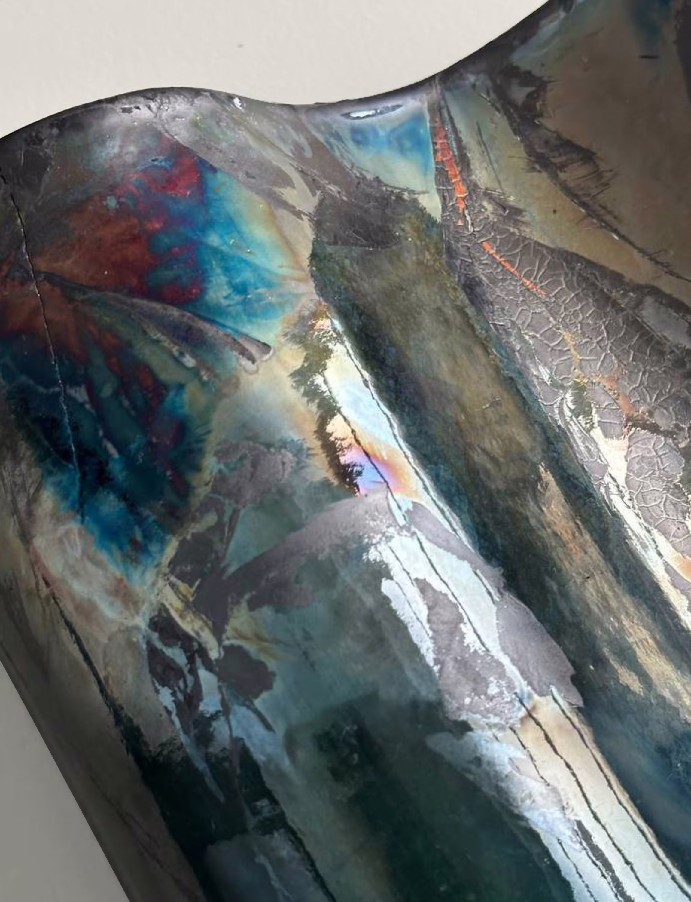 Close-up of a copper sconce with raku glaze, displaying vibrant blue, red, and metallic hues with a textured, crackled surface.