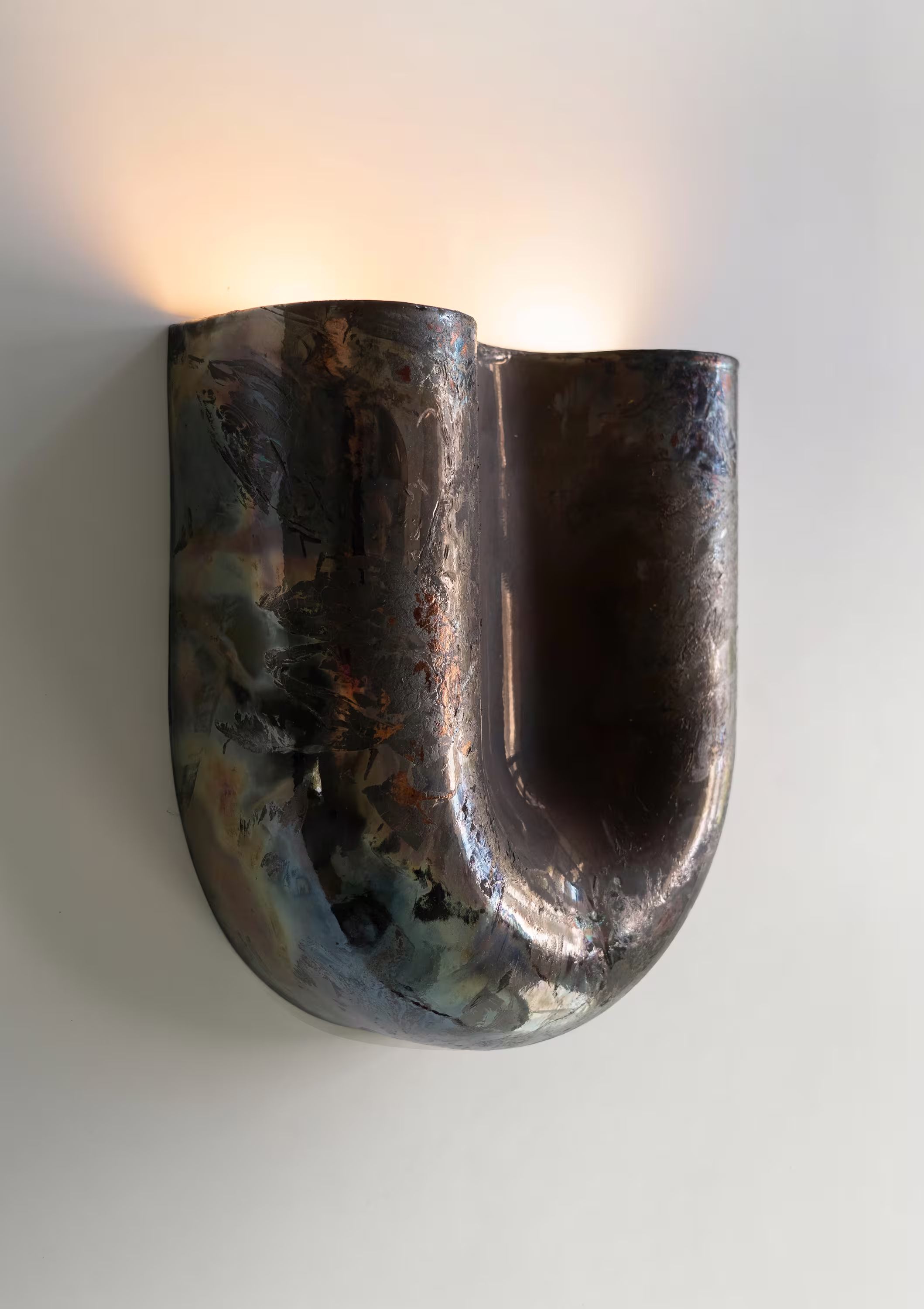 Copper sconce with raku finish, featuring a sculptural, fluid form casting warm light against a neutral wall.