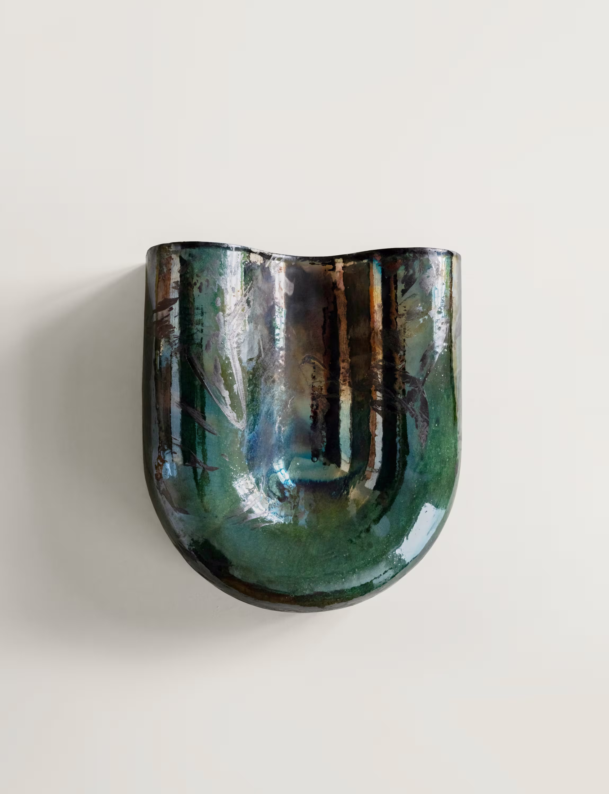 Copper sconce with a glossy raku glaze, displaying a wavy, reflective surface with green and blue tones.