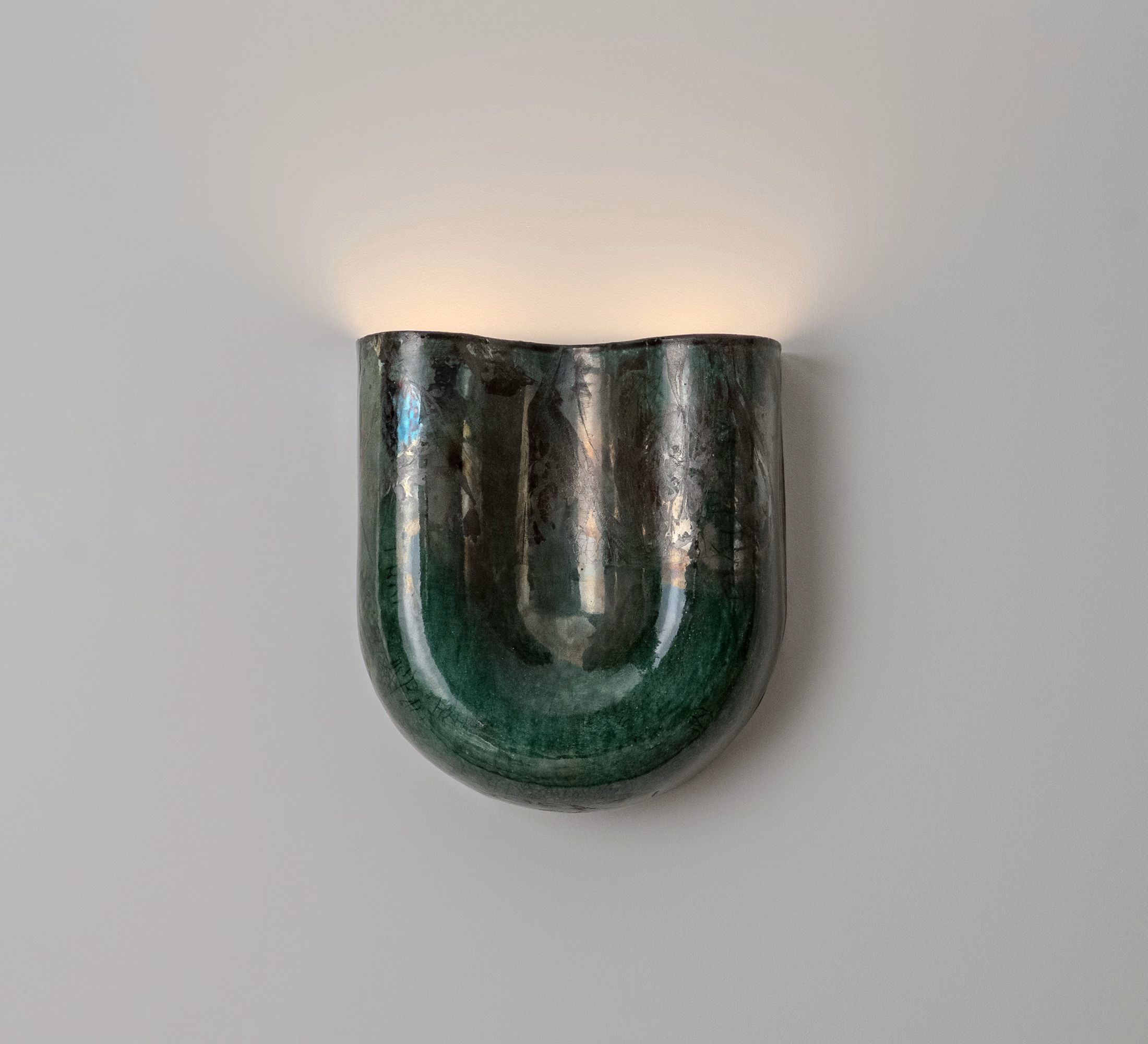 Green raku ceramic wall sconce with a rounded, glossy finish emitting soft light against a neutral wall.
